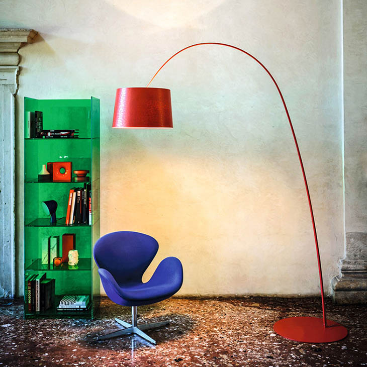 red foscarini twice as twiggy floor lamp near a blue chair and green bookshelf