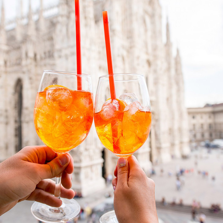 two people clinking glasses of aperol spritz in front of the duomo